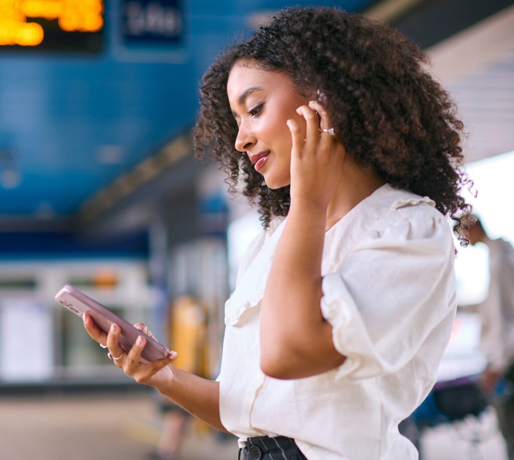Businesswoman Commuting On Train Platform Streaming Music Or Podcast From Mobile Phone